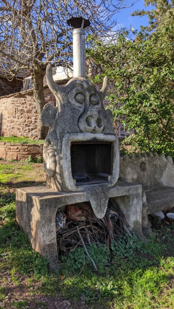 Sculpture de 2.5 m de haut dans le jardin servant de barbecue. Elle représente un monstre, la bouche ouverte sert de foyer pour le barbecue. Il a 2 cornes sur les côtés, il tire la langue, à 2 grandes oreilles et une cheminée en zinc dépasse de sa tête