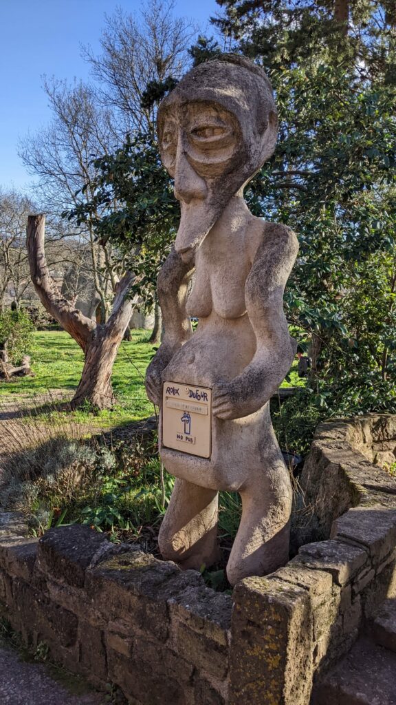 Sculpture à la chaux de 3 m de haut, indépendante et représentant une statue africaine. La bouche part en pointe vers le bas du visage, dans son ventre est logé la boite aux lettres.