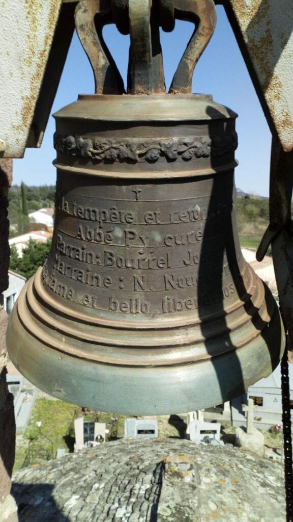 Gros plan sur la cloche de l'église. On peu lire une série d'inscription gravée sur la cloche.