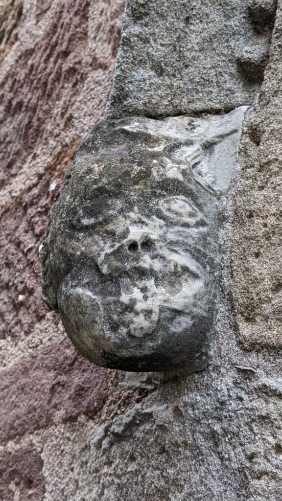 Tête d'un personnage grimaçant sculpté, possiblement d'origine wisigoth, d'environ 20 cm de haut servant de culot sous l'arche du portail de l'église Ste Marie de Frangouille. Visage abîmé par le temps