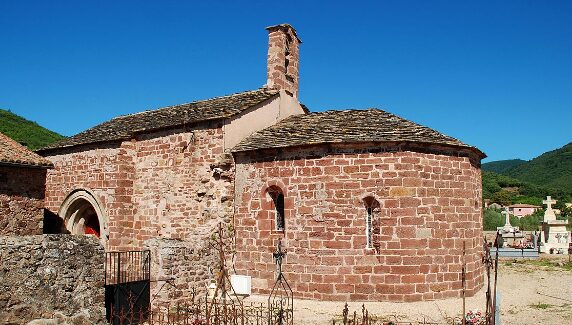 Photo de l'église Ste Marie de Frangouille (prise depuis le cimetière) . Ciel bleu, vue sur quelques tombes, construction de l'église avec son petit clocher en pierre de gré rouge.