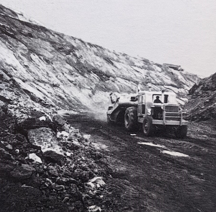 Photo noir et blanc. Un engin de chantier (pelle) sur une piste devant un mur de charbon lors de l'extraction dans la mine découverte