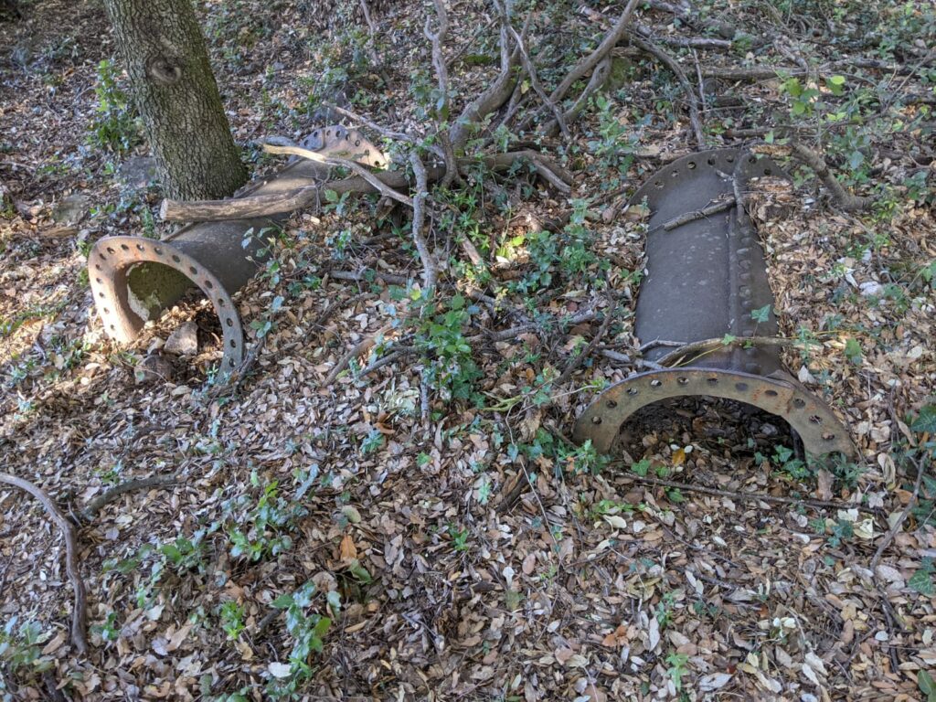 Deux vieux tuyaux rouillés d'environ 1 mètre posé sur le sol d'une foret au milieu des feuilles et branches près d'un tronc d'arbre