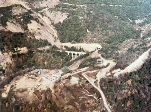 Ancienne photo un peu jaunie. Vue au milieu sur le viaduc, devant sur la zone technique avec un hangar. Autour une partie de la montagne est pellé (trace de la mine découverte). le reste est recouvert de végétation